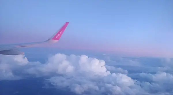 Skrzydło samolotu Wizz Air nad chmurami, wczesny poranek. Czas na loty do Anglii!