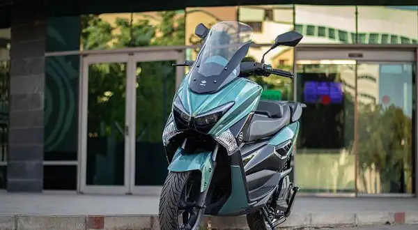 Scooter onex motos color verde menta, con parabrisas alto, estacionada frente a un edificio moderno con puertas de cristal.