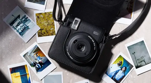 Czarny aparat Instax w futerale, otoczony natychmiastowymi zdjęciami. Dowiedz się, jak robić zdjęcia Instax, tworząc własne wspomnienia.