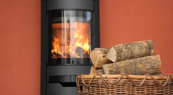 Moderner Kaminofen mit brennendem Holz. Ein Korb mit Holzscheiten daneben. Erneuerbare Energien, 15 Prozent Holz als Brennstoff.
