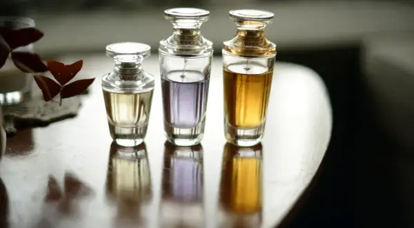 Trzy eleganckie flakoniki perfum o różnej zawartości i kolorze płynu, stojące na drewnianym stole.