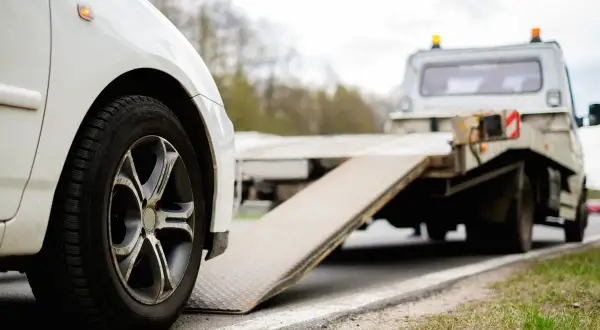 Białe auto na lawecie. Wygląda na to, że to szkoda całkowita w leasingu, auto jest zabierane przez pomoc drogową.