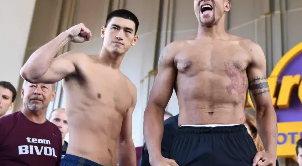 Two boxers face off. One, wearing a "team BIVOL" shirt, flexes his bicep. The other, with tattoos, shouts. Bivol fights in the light heavyweight class.