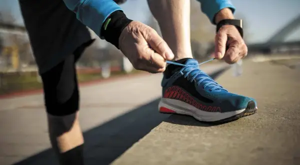 Un coureur attache ses lacets bleus, prêt à laisser une trace de frottement chaussure sur le bitume.