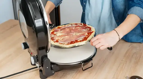 Osoba wkłada pizzę z szynką do pieca. To dopiero początek, bo zaraz dodamy ulubione dodatki do pizzy!