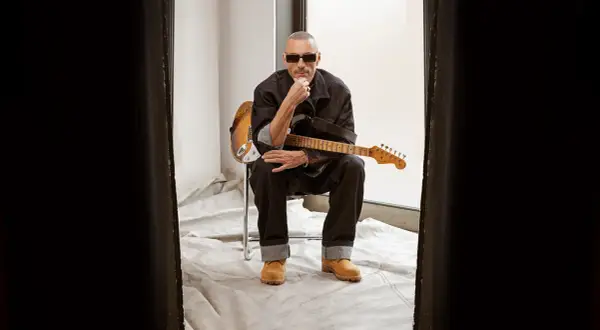 Alex Britti, con occhiali da sole e chitarra, sembra pensieroso, quasi gelido, mentre riflette sui suoi testi.