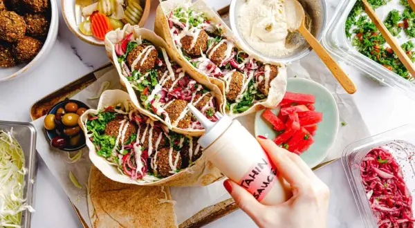 Leckeres Falafel-Rezept: Pita gefüllt mit Falafel, Salat, roten Zwiebeln und Tahini-Sauce. Dazu Hummus, Oliven und eingelegtes Gemüse.