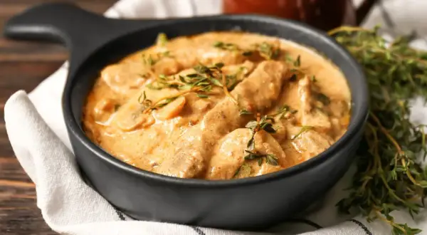 Cremiges Rindfleisch mit Pilzen, garniert mit frischem Thymian. Ein köstliches stroganoff rezept original, serviert in einer schwarzen Schüssel.