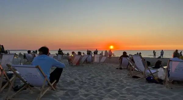 Zachód słońca międzyzdroje. Ludzie siedzą na leżakach na plaży, obserwując pomarańczowe niebo i morze.