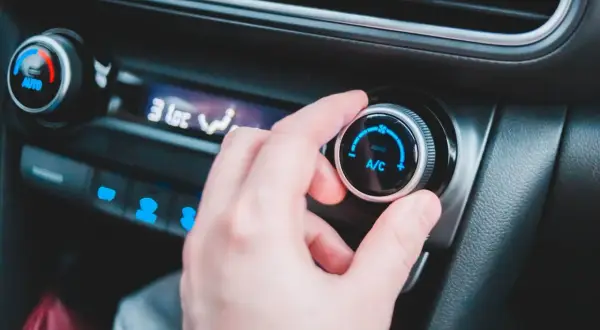 En hand vrider på reglaget för ac i bilen. Temperaturen sjunker snabbt.