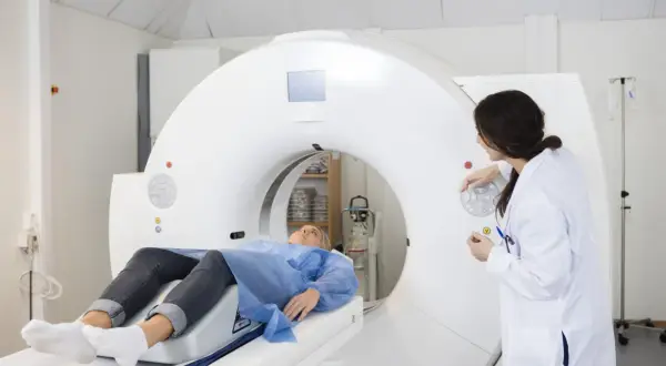Pacjentka leży na stole tomografu komputerowego, a lekarka przygotowuje badanie. Dowiedz się, ile trwa tomografia komputerowa.