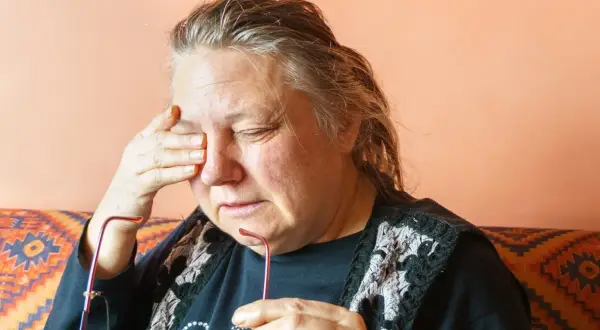 Kobieta z zamkniętymi oczami, pocierająca skroń. Może to być jeden z objawów stwardnienia rozsianego, takich jak zmęczenie czy bóle głowy.