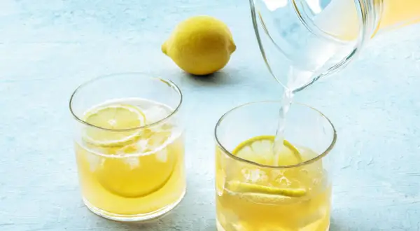 Erfrischendes Wasser mit Zitrone wird morgens in ein Glas mit Eis und Zitronenscheiben gegossen.