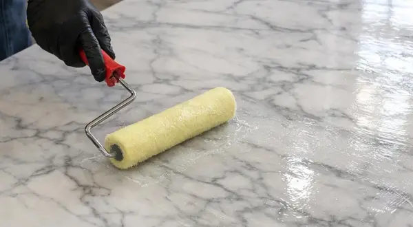 Mano guantata applica resina epossidica per marmo con un rullo, creando una finitura lucida e protettiva.