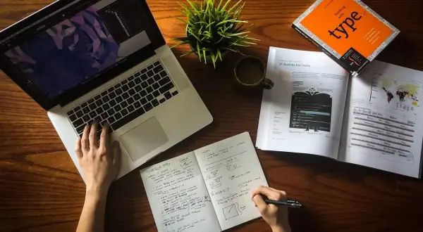 Ręce pracują nad projektem, laptop, notatnik i książka o typografii. To idealne warunki do start up.