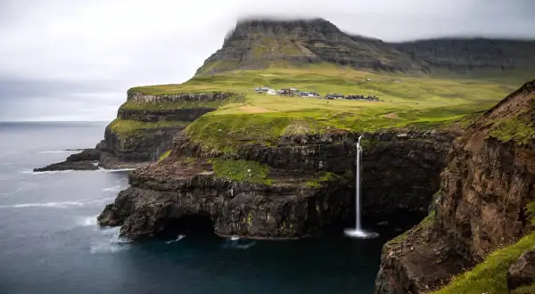 Paysage spectaculaire des îles Féroé : une cascade tombe d'une falaise verdoyante dans l'océan. Idéal pour une randonnée inoubliable.