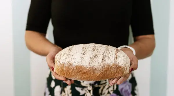 Kobieta trzyma bochenek chleba razowego. Zastanawiasz się, ile kcal ma kromka chleba razowego? Ten pyszny chleb może być częścią zdrowej diety.