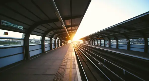 Pusta stacja kolejowa o zachodzie słońca. Długie tory kolejowe i peron pod zadaszeniem. Może to czas na złożenie wniosku o odszkodowanie za opóźnienie pociągu?
