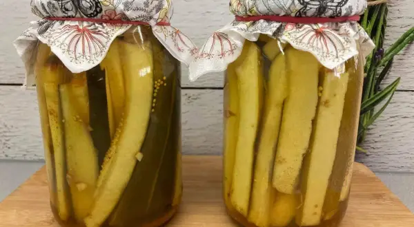 Dwa słoiki z cukinią w zalewie słodko-kwaśnej z curry. W tle gałązka rozmarynu.