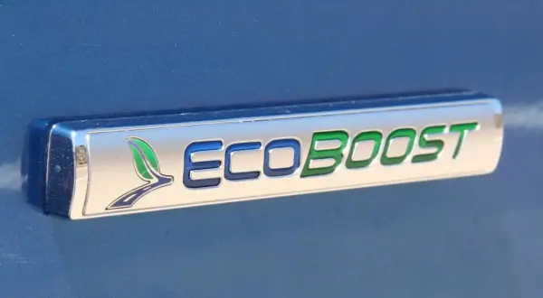 Ford Focus 1.0 EcoBoost kamremsbyte pris. Ett emblem på en blå bil visar "ECOBOOST" med gröna och blå bokstäver.