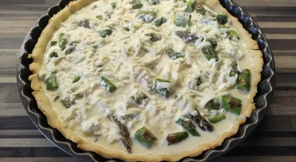Tarta ze szparagami, gotowa do pieczenia, z kremowym nadzieniem i serem.