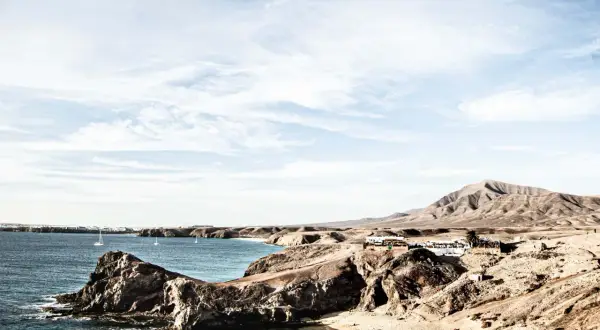 Surowe krajobrazy wulkaniczne Lanzarote, gdzie skutki braku zapasu wody są widoczne na trasach turystycznych, kontrastują z błękitem oceanu i białymi żaglami.