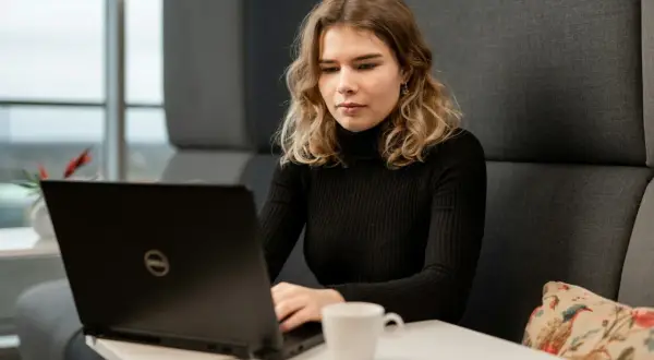 Młoda kobieta z wrodzonymi zdolnościami do pracy przy laptopie, skupiona na zadaniu. Obok filiżanka kawy.