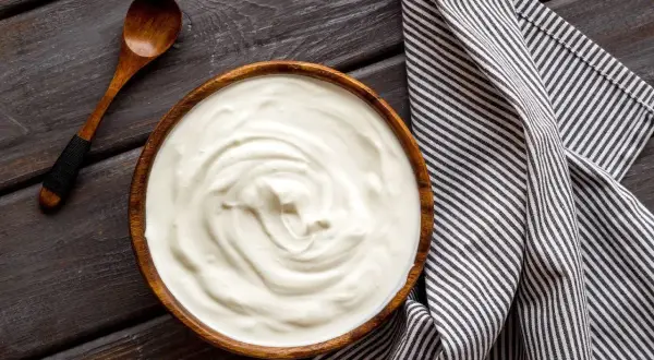 Prosty krem z mascarpone i jogurtu w drewnianej misce, obok drewniana łyżka i pasiasty ręcznik.