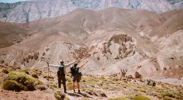 Deux randonneurs bras ouverts contemplent un paysage désertique spectaculaire lors d'une randonnée Atlas Maroc. D'autres marcheurs sont visibles au loin.