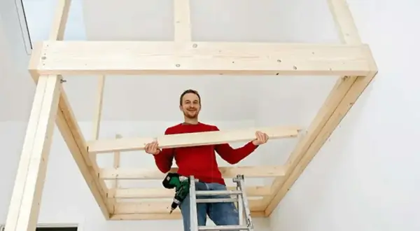 Man på en stege håller en träplanka, redo att bygga en stege till en loftsäng.