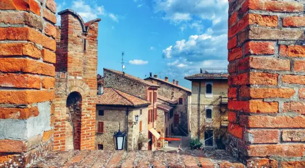 Un antico borgo vicino Parma, con case in pietra e tetti rossi, incorniciato da mura di mattoni sotto un cielo azzurro e nuvoloso.