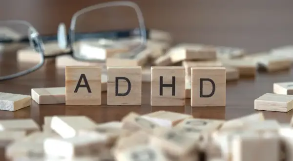 Drewniane klocki z literami "ADHD" i rozrzucone po stole, sugerujące poszukiwanie rozwiązań, np. leki na ADHD.