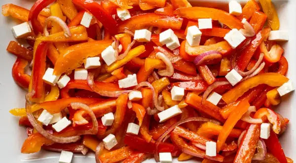 Bunter Paprika Salat mit roten Zwiebeln und weißen Würfeln, wahrscheinlich Feta-Käse.