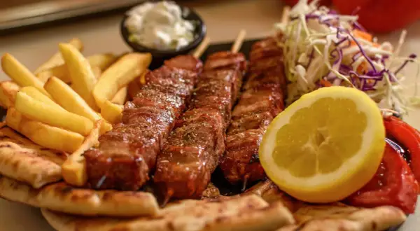 Pyszne souvlaki na patykach, podane z frytkami, pitą, sałatką i cytryną.