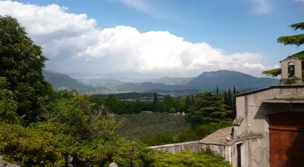 Panoramica sul percorso eremo dei camaldolesi Bardolino, con vista su colline, uliveti e montagne sotto un cielo nuvoloso.