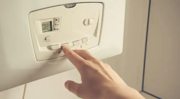 Main d'une personne appuyant sur les boutons d'une pompe à chaleur. Faut-il éteindre sa pompe à chaleur l'été ?