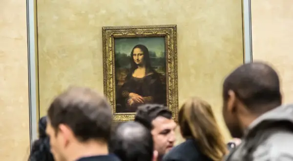 Mona Lisa z Isleworth, otoczona tłumem widzów, spogląda tajemniczo ze złotej ramy.