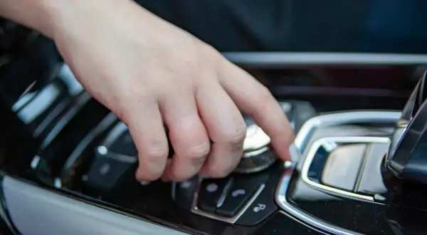 Main d'une personne actionnant un bouton sur la console centrale d'une voiture, peut-être pour savoir comment débloquer un frein à main automatique.