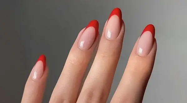 Dłonie z paznokciami w kształcie migdałków, ozdobione klasycznym french manicure z intensywnie czerwonymi końcówkami.