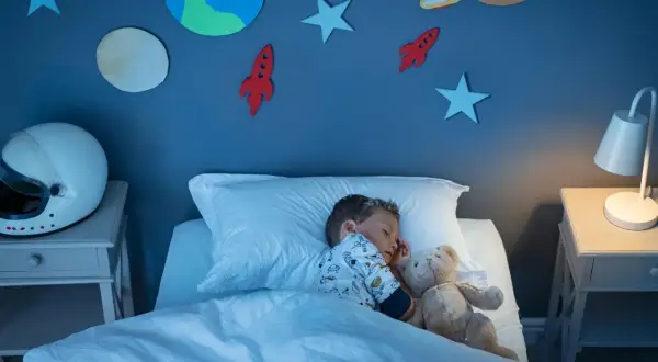 Kleiner Junge schläft im Weltraum-Kinderzimmer. Die kinderzimmer wandgestaltung mit Planeten und Raketen inspiriert Träume von Abenteuern.