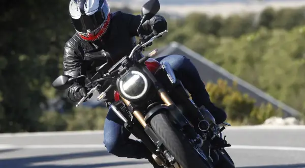 Motociclista con casco Venom en pleno rodaje moto, inclinado en una curva con paisaje verde de fondo.