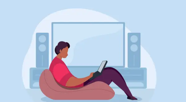 Person im Sessel mit Laptop, vor einem großen Bildschirm und Lautsprechern. Ein Beispiel für hybrides Arbeiten, flexibel und bequem.
