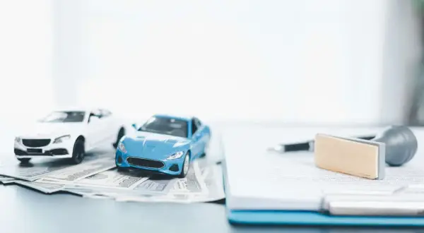 Modellini di auto su banconote, con documenti e timbro. Pensando a come disdire assicurazione auto prima della scadenza.