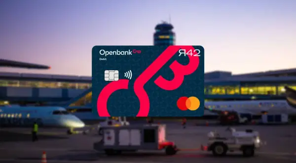 Openbank Debitkarte mit Mastercard-Logo vor einem Flughafen bei Dämmerung. Gute Openbank Erfahrungen für Reisen.
