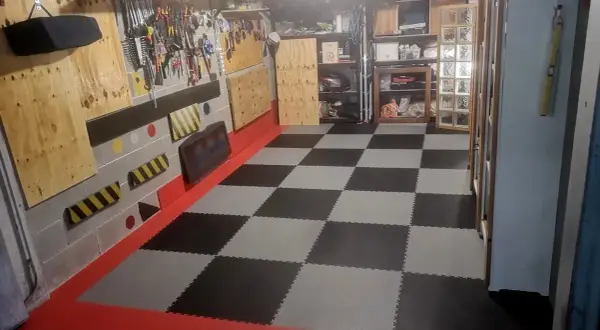 Pavimento a scacchi in piastrelle carrabili per garage, con bordi rossi e pareti attrezzate per gli attrezzi.