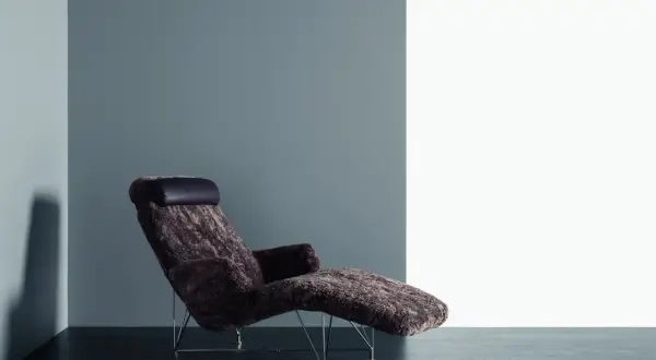 En DUX Superspider fårsinn-klädd fåtölj med mörk läderkudde står på ett mörkt trägolv mot en grå och vit vägg.