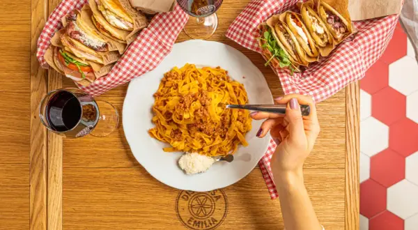 Tagliatelle al ragù, un classico italiano. Accanto, piadine farcite e un bicchiere di vino rosso.