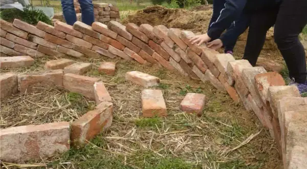 Costruzione di un keyhole garden con mattoni. Mani che posizionano i mattoni per creare la forma circolare.