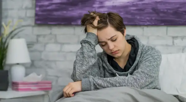 Müde Person im Bett, die sich an den Kopf fasst. Mögliche Anzeichen von Blutkrebs wie Müdigkeit und Kopfschmerzen sollten ernst genommen werden.