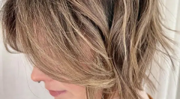 Kobieta z brązowymi, rozjaśnianymi pasmami i lekko potarganymi, shaggy hair.